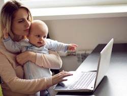 Mom on maternity leave holding her baby and using the laptop