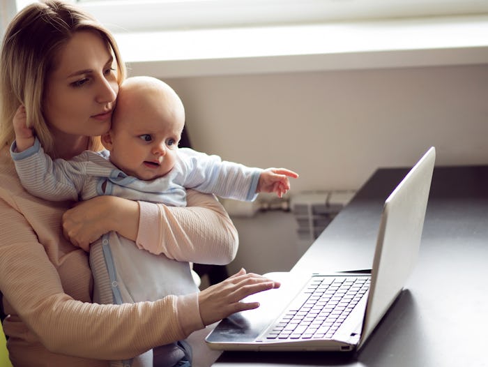 Mom on maternity leave holding her baby and using the laptop