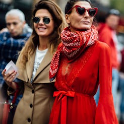 Two women representing street-style fashion walking through a crowd looking their way.