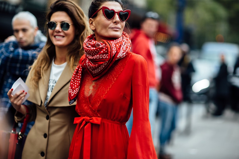 Two women representing street-style fashion walking through a crowd looking their way.