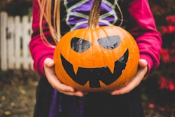 A closeup of a child in a Halloween costume, holding a painted pumpkin