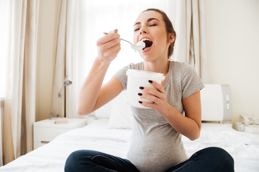 A pregnant woman eating an ice cream while sitting on the bed