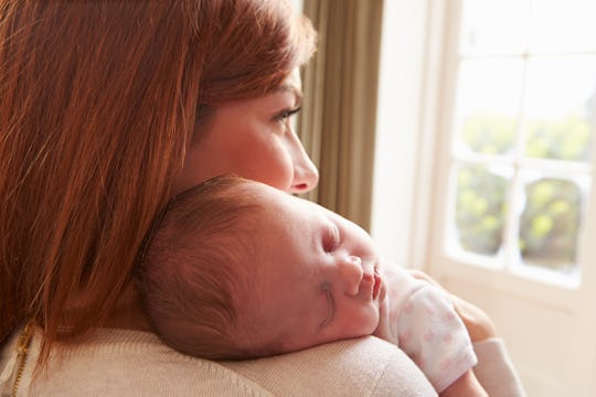 A new mom standing and holding her sleeping newborn baby