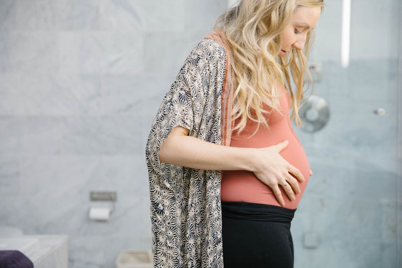 Pregnant woman standing in the bathroom and holding her belly