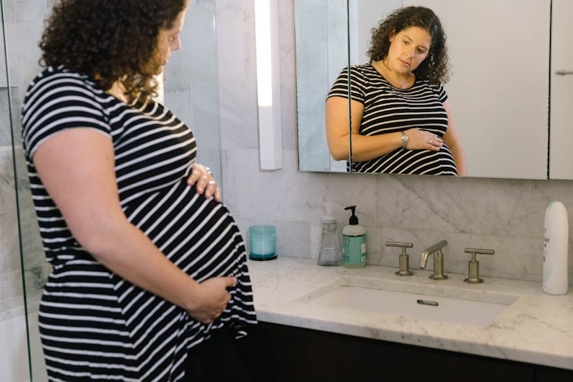 Pregnant woman standing in front of the bathroom mirror and holding her belly