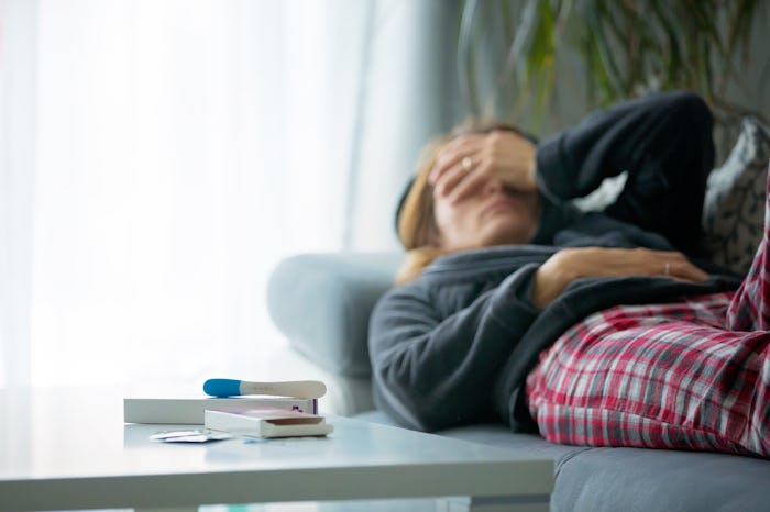 A woman lying on the couch, closing her eyes, with a pregnancy test on the table next to her