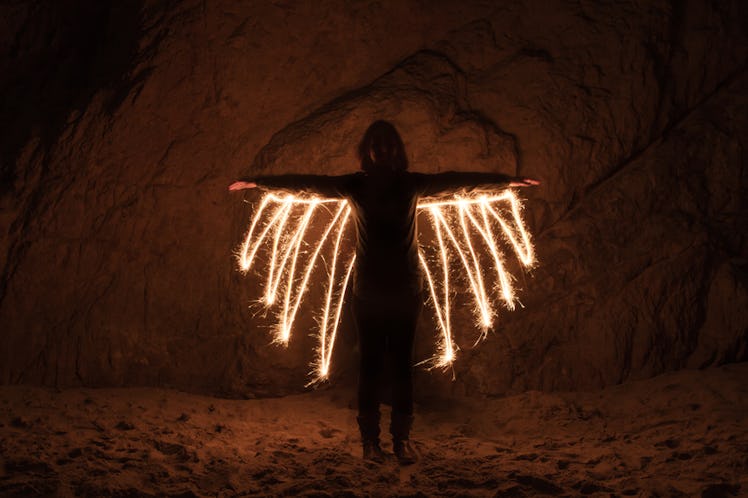A woman in a dark space with her arms wide open and light-effect created lines under her arms as win...