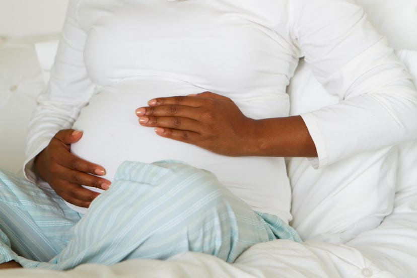 A pregnant woman sitting on her bed, caressing her stomach