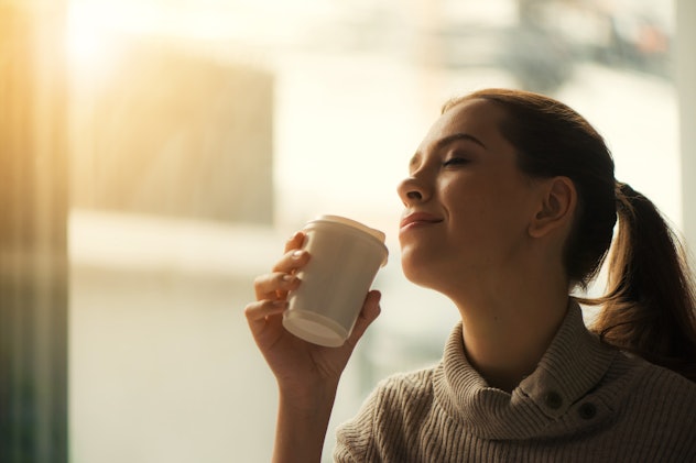 A woman rocking the ponytail, holding the cup of coffee and posing for the picture