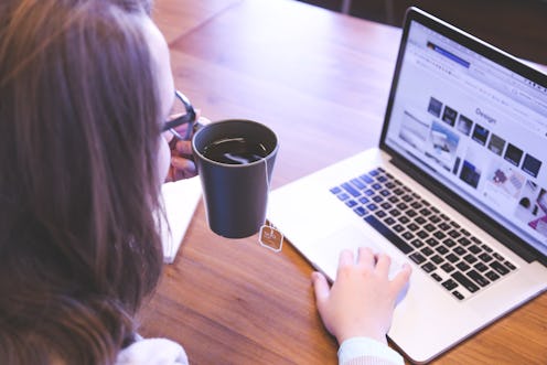 A woman looking at her personal website on her laptop while holding a cup of coffee