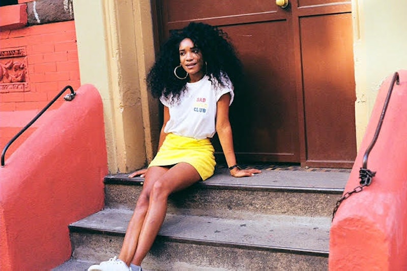 Elyse Fox, founder of Sad Girls Club, sitting on stairs in a yellow skirt and white shirt