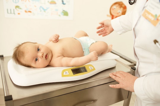 A baby with a tongue-tie lying on a weighing machine in doctor's office.