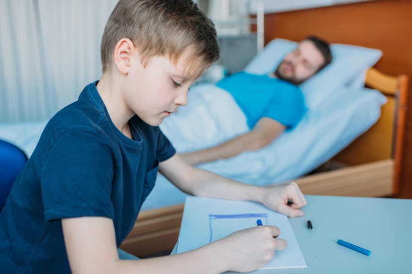 young boy writes note while father lies in bed