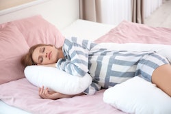 A woman lying in bed in striped pajamas hugging her pregnancy pillow