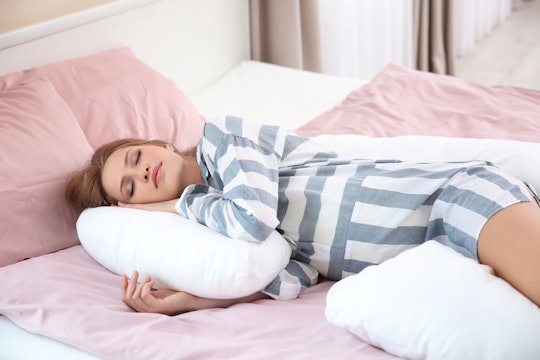 A woman lying in bed in striped pajamas hugging her pregnancy pillow