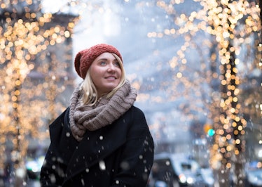 A blonde woman in a beanie cap, scarf, and jacket smiles while snow falls during winter in New York ...
