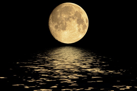 huge full moon on horizon of water, reflecting on black water