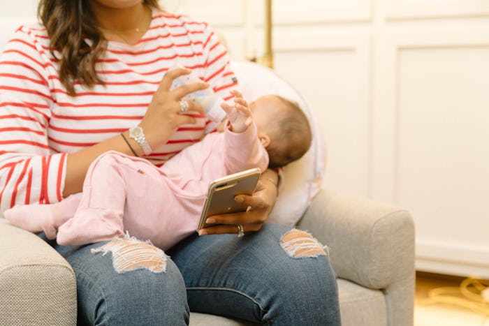 A work at home mom looking at her phone while bottle feeding her baby