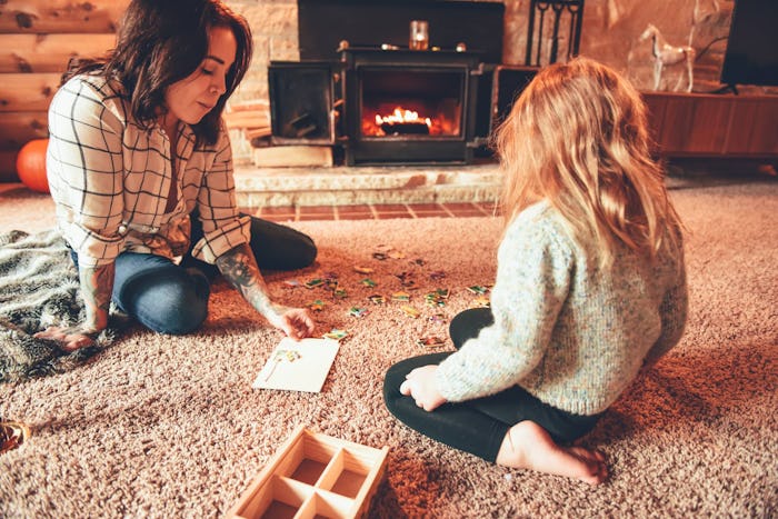 A woman and her daughter sitting on a carpet in front of fireplace playing games