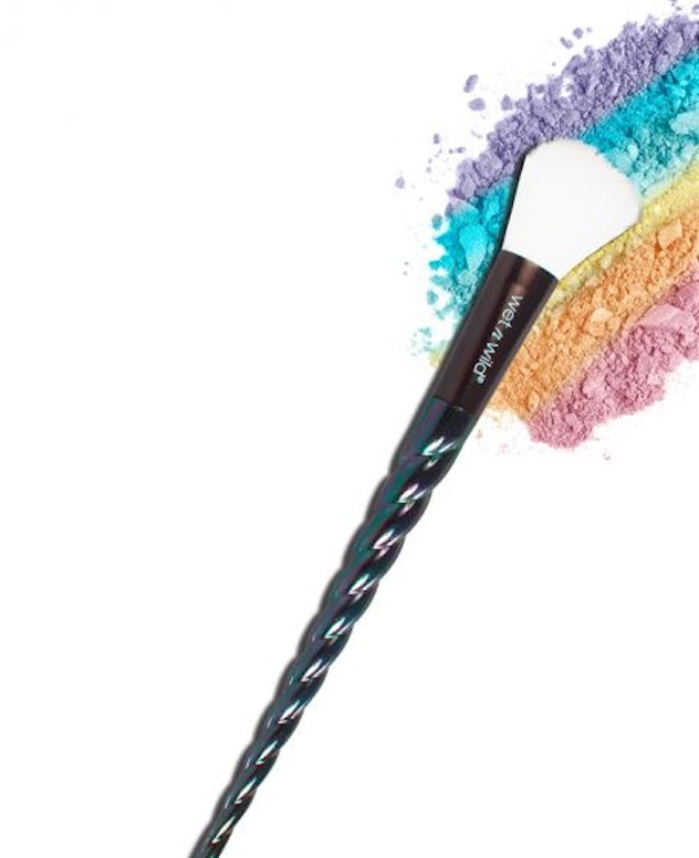 A makeup brush smearing the colorful powder on a white surface.