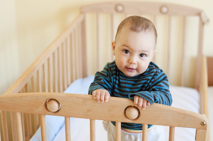 A little baby standing awake in a baby bed