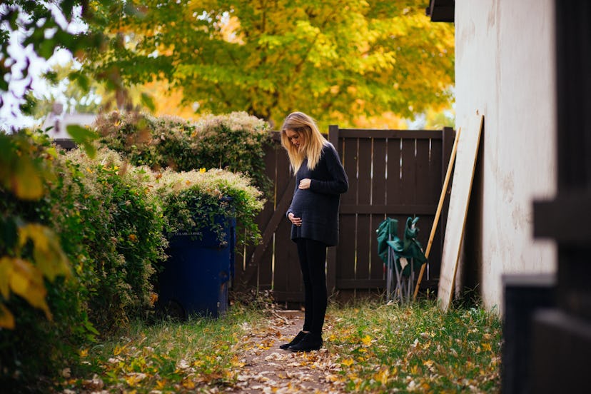 Woman standing in her back yard with her hand on her belly 