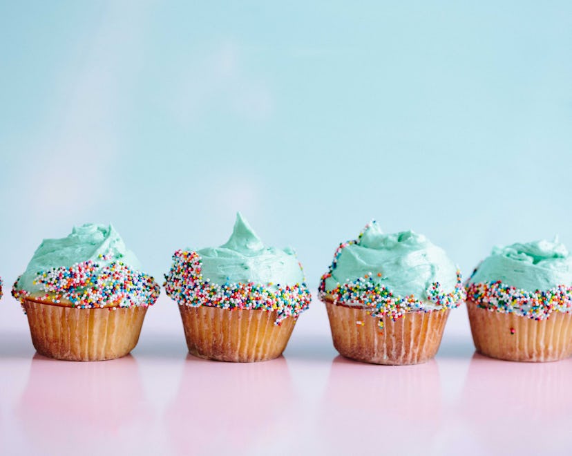 4 sugar frosted cupcakes placed on a pink table in front of a blue backdrop.