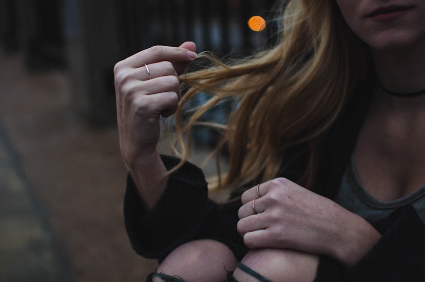 Woman sitting outside at night touching her hair which is falling out