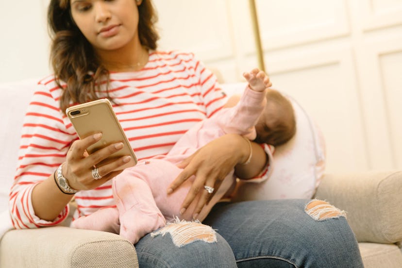 A mother looking at the phone while holding her baby