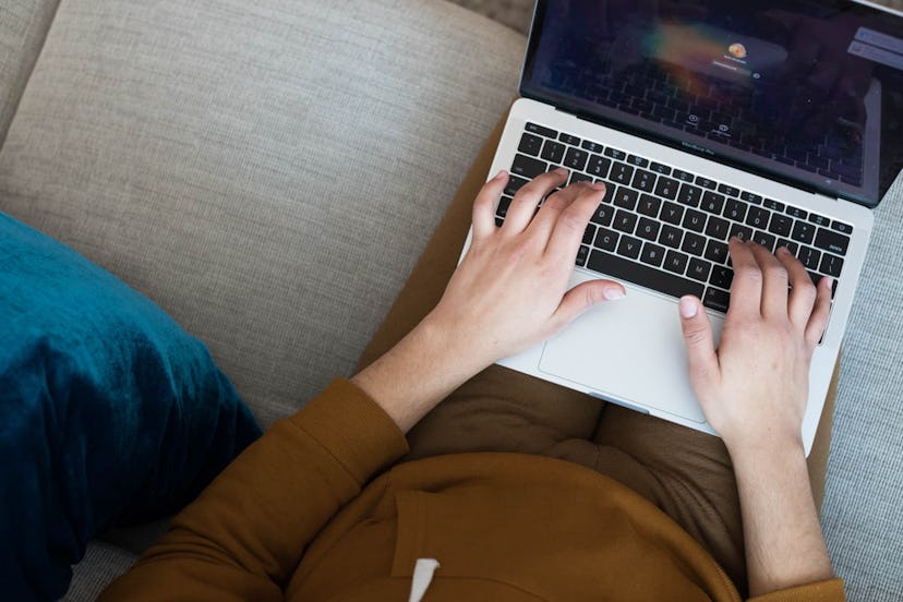 Woman sitting on the couch with a laptop on her lap, typing .