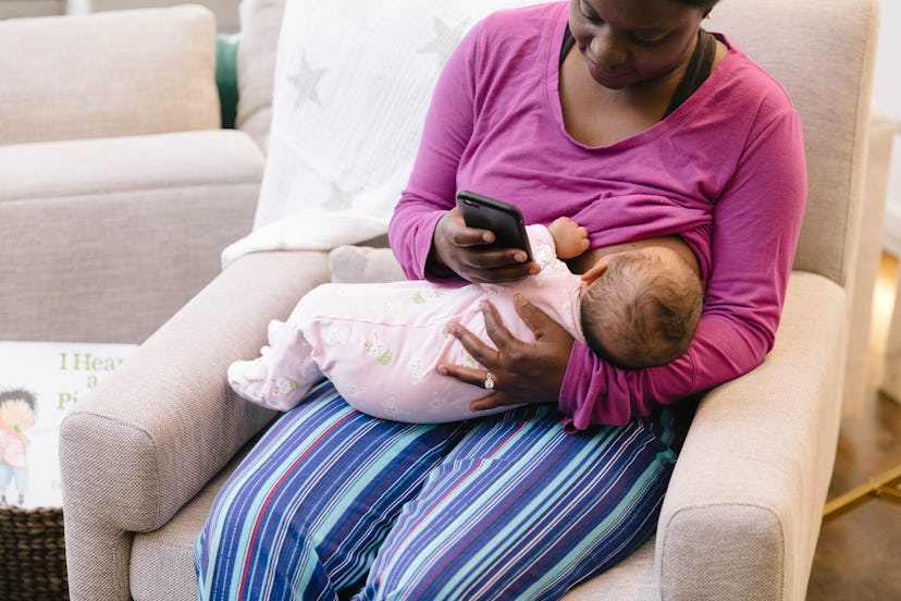 A mother breastfeeding her baby while looking at her phone