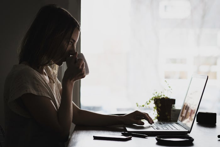 A working mom drinking a cup of coffee and sitting at her laptop as she returned to work after givin...