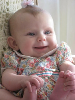 A little baby holding her feet and smiling while laying on the bed