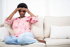 A woman sitting on a couch and holding her head with hands because of headache