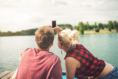 A couple taking a selfie while sitting on a dock next to a lake