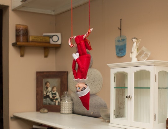 an elf on the shelf doll hanging upside down from a candy cane