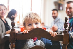 a little boy peeking over the back of a chair at the thanksgiving dinner table