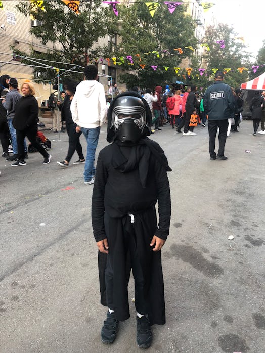 A little boy wearing a black costume and a mask helmet with a hood