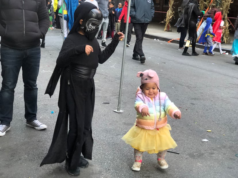 A little boy wearing a black costume and a mask helmet with a hood while standing next to his little...