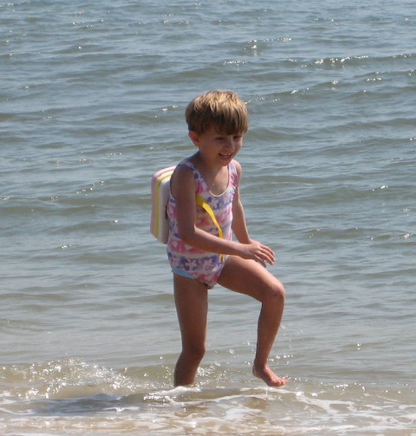 A little girl jumping in the water at the beach.