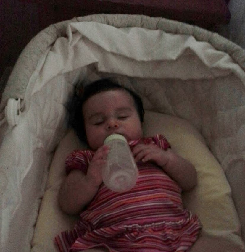 A little girl holding her bottle while sleeping in her baby bed