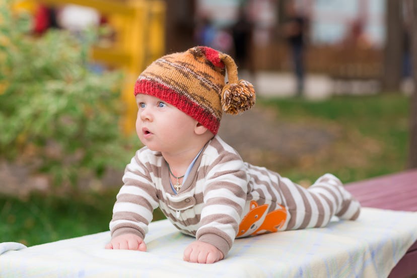 Baby laying outside on a blanket, wearing a hat, in a story about how to dress baby for cold tempera...