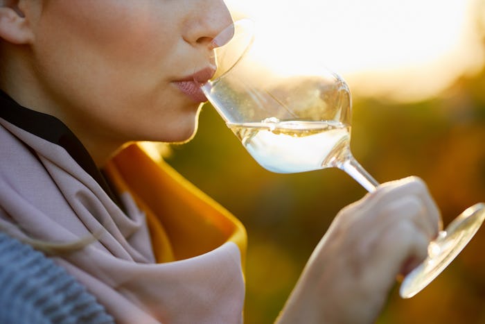 A woman drinking white wine with a sun setting in her background