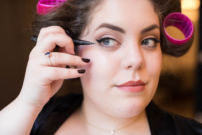 A woman with pink hair rollers putting her makeup for New Year's Eve party