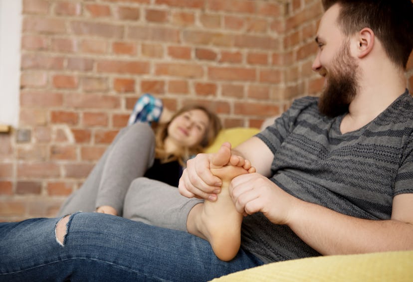 A guy massaging his partner's feet while she's lying on the couch
