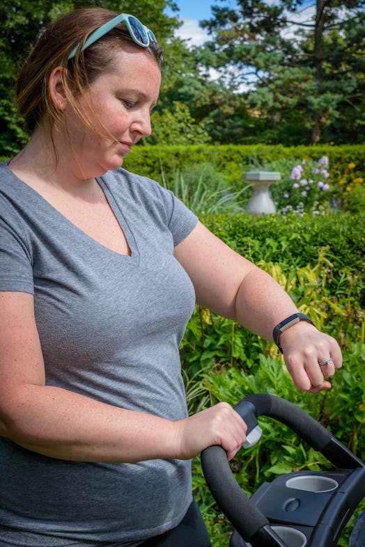 A woman in a gray t-shirt is looking at her watch while pushing the baby stroller