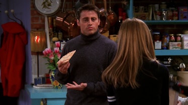Rachel looks at Joey while he holds up a slice of pizza in 'Friends.'