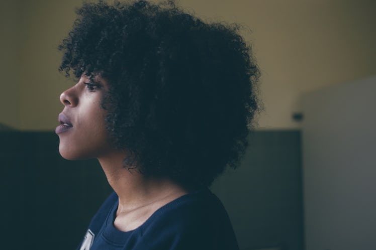A curly-haired woman in a navy sweater looking through a window and cold weather affects her stress ...