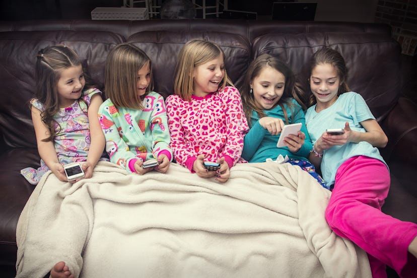Four young girls in their pajamas are sitting on the couch and looking into their phones
