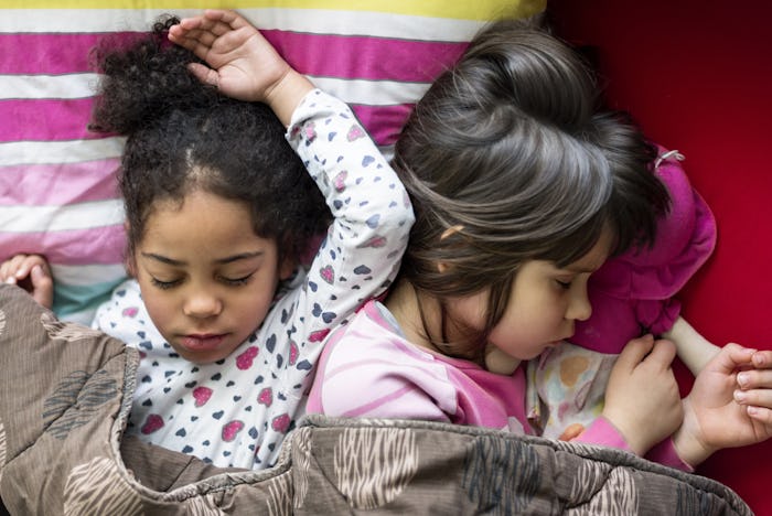 Two little girls sleeping under the covers together during a sleepover